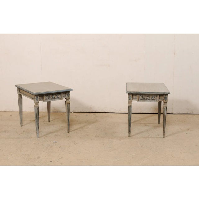 An Italian pair of carved and painted wood side tables. This vintage pair of tables from Italy each have rectangular-...