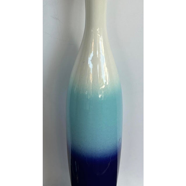 each slender bottle-form ceramic lamp with graduated glazed surface of ivory, aqua and cobalt blue; all resting on a round...
