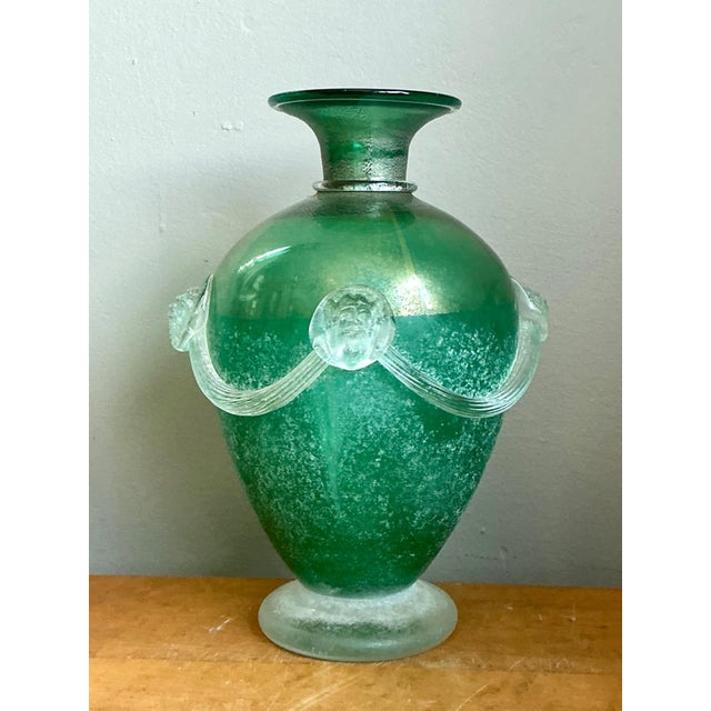 This vintage green art glass vase, expertly crafted in blown glass, showcases intricate relief work of stylized faces...