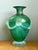 This vintage green art glass vase, expertly crafted in blown glass, showcases intricate relief work of stylized faces...