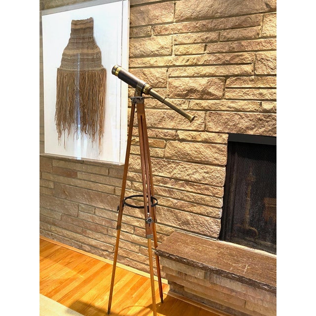 A brass and leather-wrapped telescope mounted on a wooden tripod stand. The eyepiece, focusing shaft, lens and mounting...
