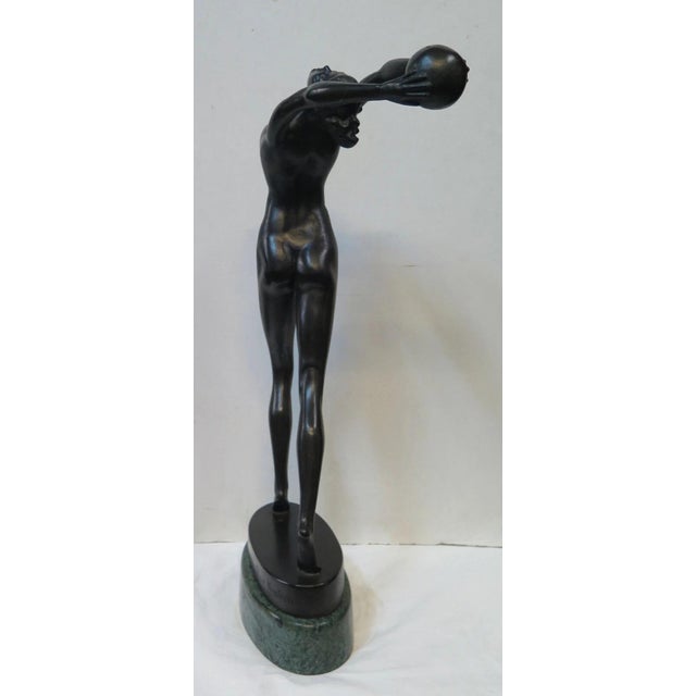 This patinated bronze sculpture of a young girl posed with a ball is signed & dated, "Olive Kooken 1930". It depicts a...