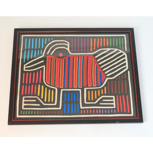 This framed Mola textile artwork features a stylized bird design with vibrant vertical stripes. The "Mola" is part of the...