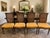 A handsome set of four vintage Neoclassical dining chairs featuring elegant cane backs, warm walnut-toned wood frames, and...