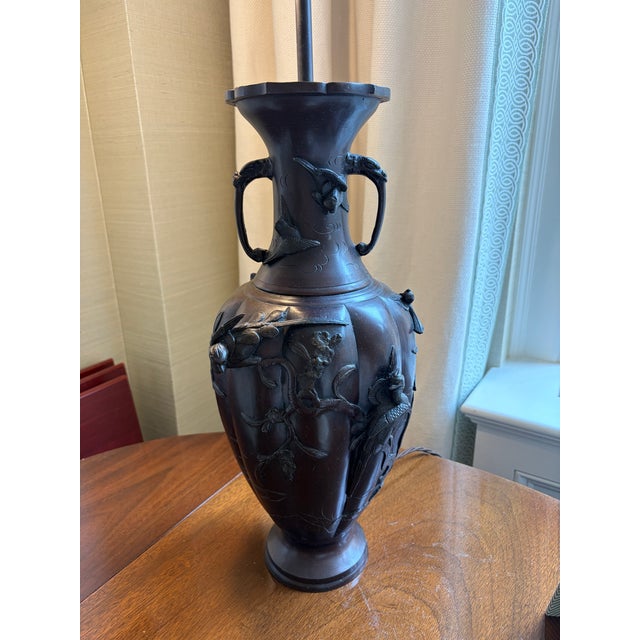 A pair of antique Japanese patinated bronze vases from the late 19th century featuring high-relief bird and floral motifs....