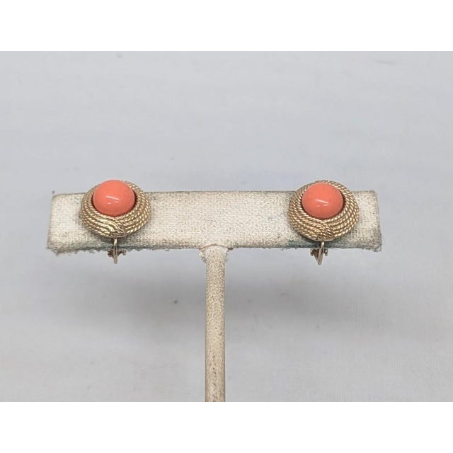 Circa 1960s small round goldtone with cabochon faux-pale orange coral center clip earrings. Marked "CINER" on clips....