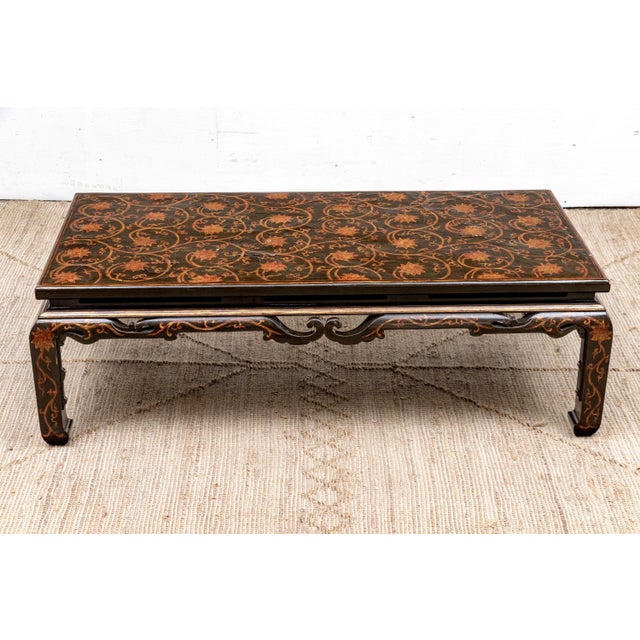 A low rectangular Chinese-style coffee table in a dark crazed and lacquered finish with a top decorated in gilt and rust-...
