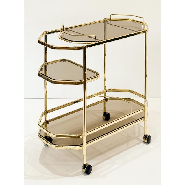 A fine Italian Modern bar cart or console drinks cart of brass and smoked glass, featuring two octagonal glass tiers and...