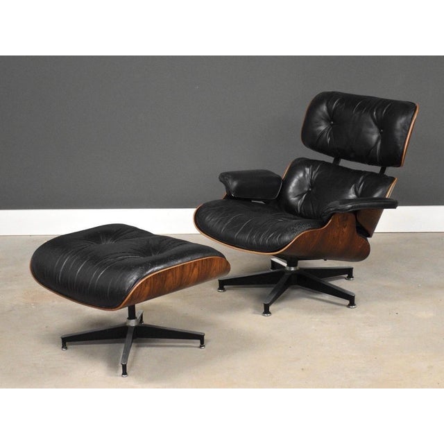A mid century modern black leather lounge chair and ottoman with Brazilian rosewood shells designed by Charles and Ray...