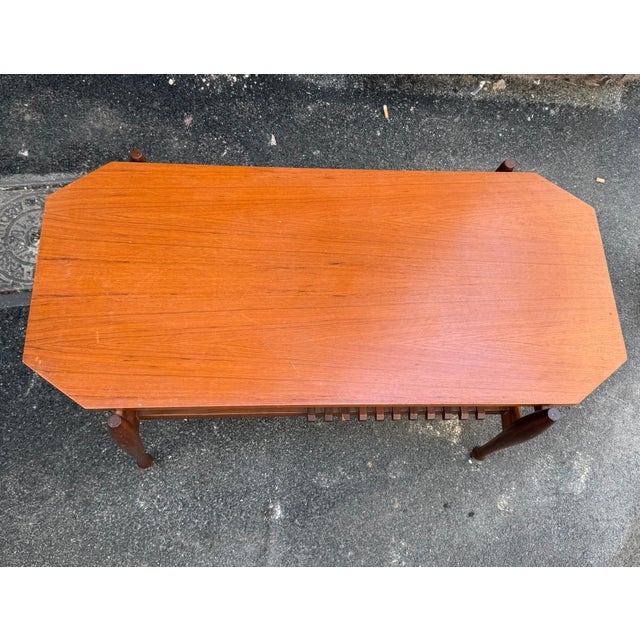 An elegant teak coffee table with a clean and refined mid-century design. The top is slightly curved with rounded corners,...
