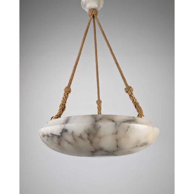 This pendant lamp reflects the Art Deco style of the 1920s, built around a wide, dish-shaped alabaster piece with dramatic...