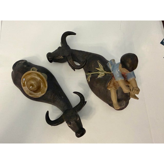 A unusual pair of buffalo with young boy appearing to ride on one of the pair and his hat along with backpack atop the...