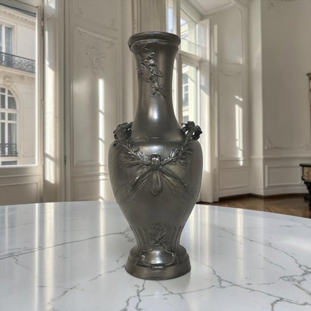 A branch of oak leaves and acorns winds down the neck of this French pewter vase, leading the eye to a sweeping garland of...