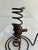 A charming spiral courting candle holder featuring a dark metal coil, adjustable wooden candle support, circular coiled...