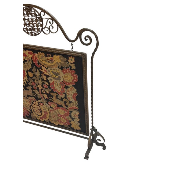 Antique iron fireplace screen featuring a floral needlepoint or tapestry panel with animal motifs set against a dark...