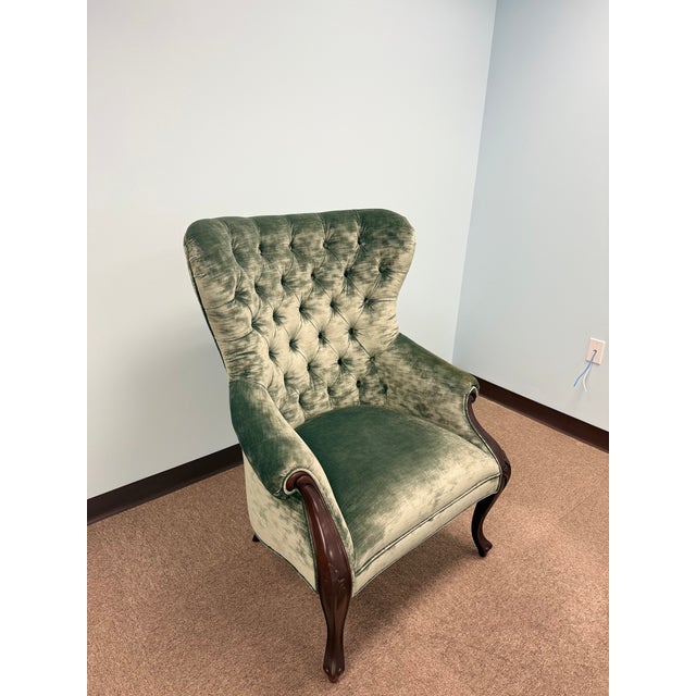Classic tufted upholstered accent chair featuring rich green velvet fabric, rolled arms, and gracefully curved wooden...