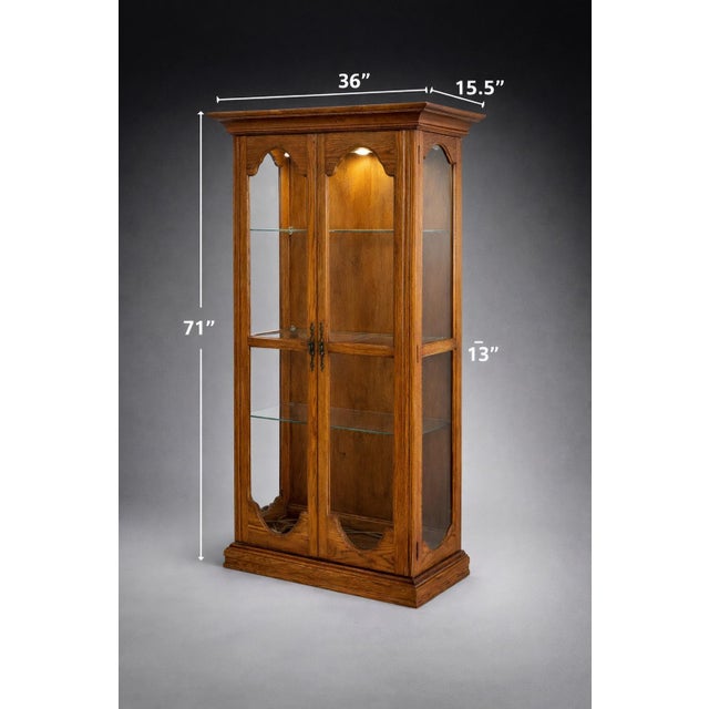 A beautifully constructed solid oak lighted display cabinet by Harbor House (Model 9630), featuring glass panels on three...