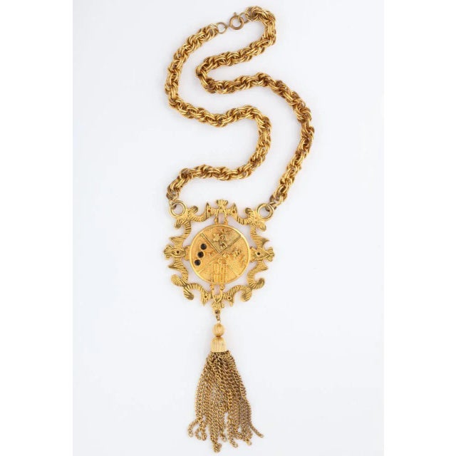 This is part of Chairish’s Costume Jewelry assortment. 1960s goldtone shield medallion necklace with large tassel and...