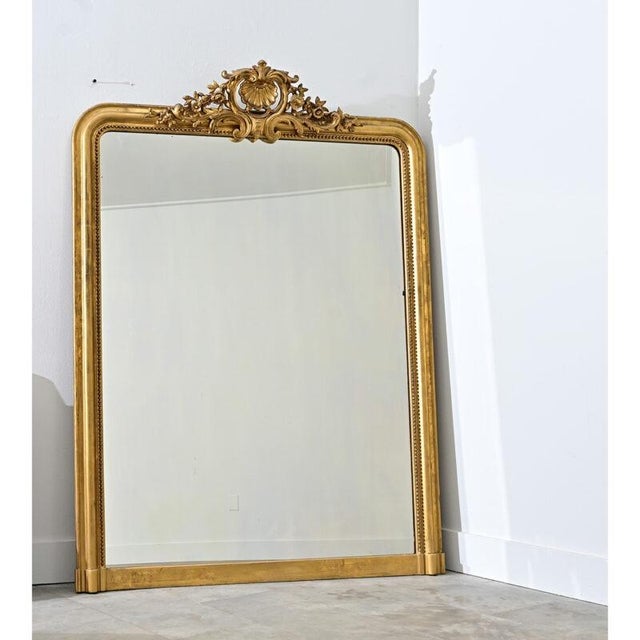 A glorious gilt mantel mirror from 19th century France with elements of baroque flamboyance at the crown between arched...