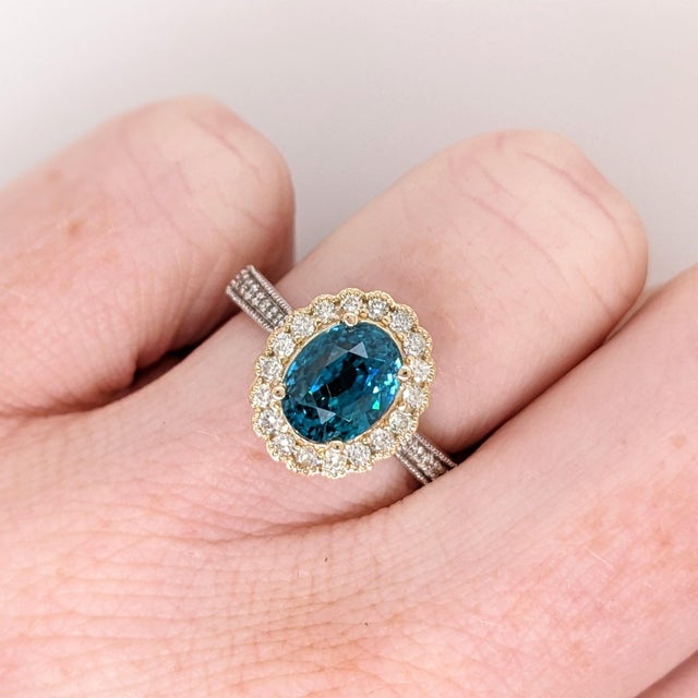 A blue zircon rests in a brilliant electric blue at the heart of this solid 14K yellow gold ring, flanked by thirty-four...