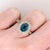 A blue zircon rests in a brilliant electric blue at the heart of this solid 14K yellow gold ring, flanked by thirty-four...