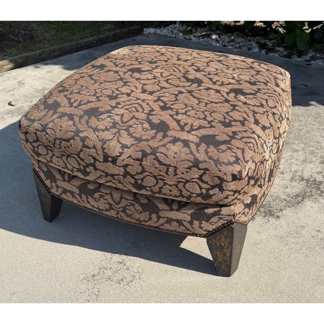 Substantial vintage upholstered ottoman featuring a generously cushioned top, richly patterned damask upholstery, and...