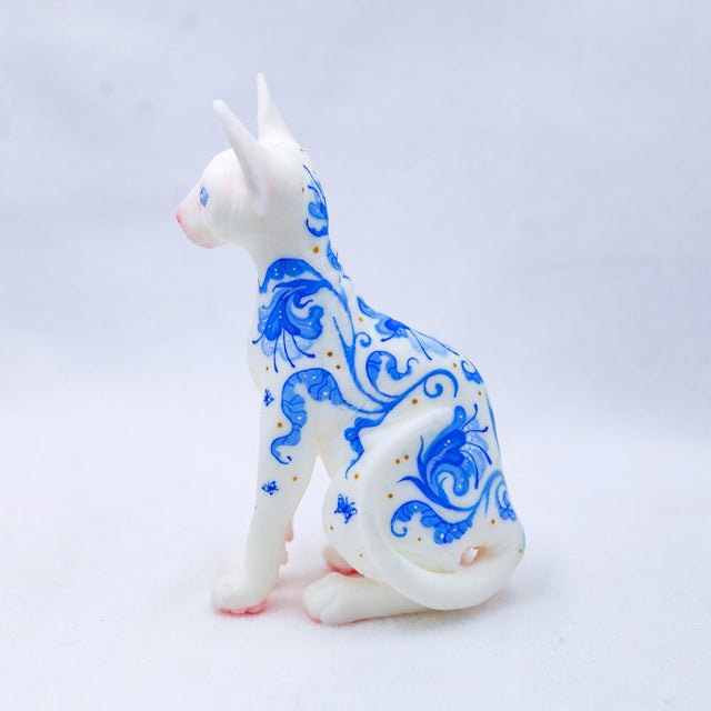 This artwork features a delicately rendered Sphynx cat, its porcelain-like surface adorned with intricate blue patterns...