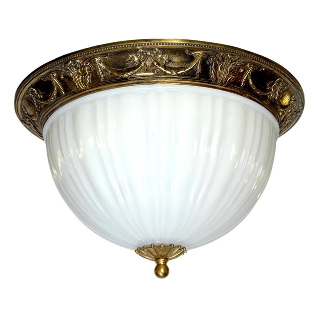 Traditional style flush mount ceiling light featuring a white fluted dome glass shade and an ornate brass fitter and...
