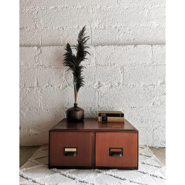 This filing cabinet from the manufacturer F&F is made of wood and features two drawers with metal handles and labeling...