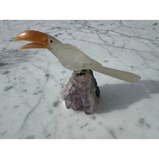 This sculpture is carved of quartz toucan stone. It depicts a parrot perched on an Amethyst Geode.