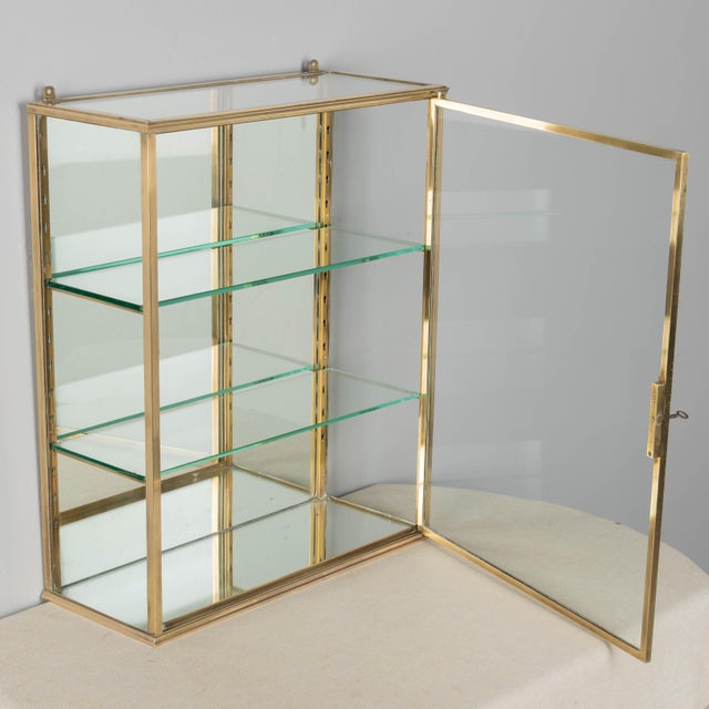 A French Art Deco hanging wall vitrine with solid brass frame, mirrored back and glass panes. Two adjustable glass...