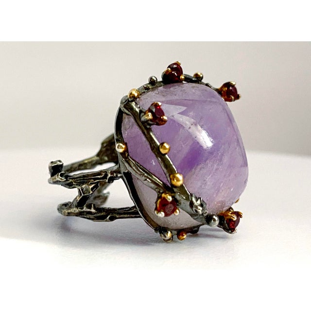 A striking, one-of-a-kind statement ring featuring a luminous cushion-cut amethyst, elegantly framed by rich rhodolite...