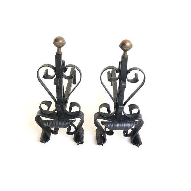 A pair of hand-forged wrought iron andirons. Expertly crafted with classic scrollwork, heart-shaped details, and elegant...