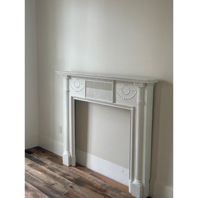 An antique neo-classical style painted pine and gesso mantlepiece. The fluted center tablet with swags of bellflowers and...