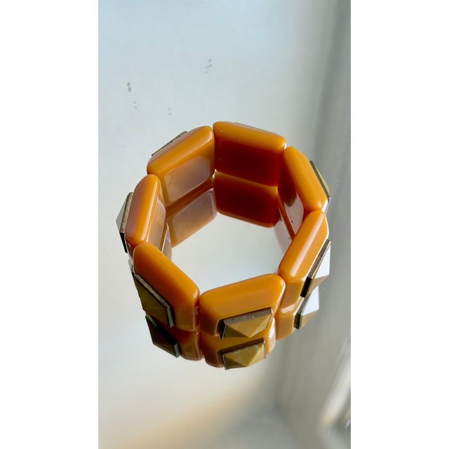 This vintage Mid-Century Modern stretch bracelet has rectangular tangerine-orange panels with gold-tone pyramid-shaped...