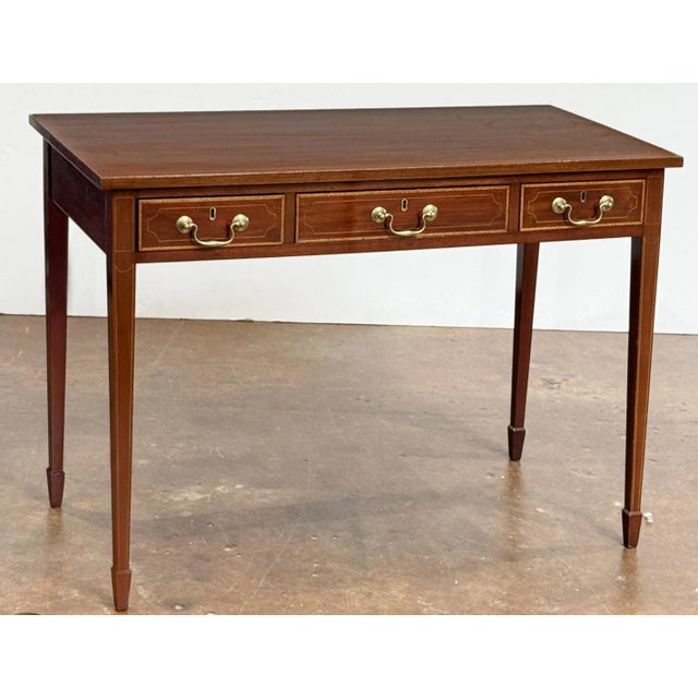 A fine English writing table or desk of mahogany from the Edwardian Era, featuring a rectangular top with inlay along the...