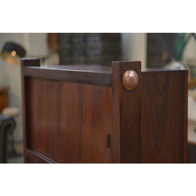 A 1950s wooden secretary desk with a clean, vertical design. The front is divided into two parts: a closed upper...