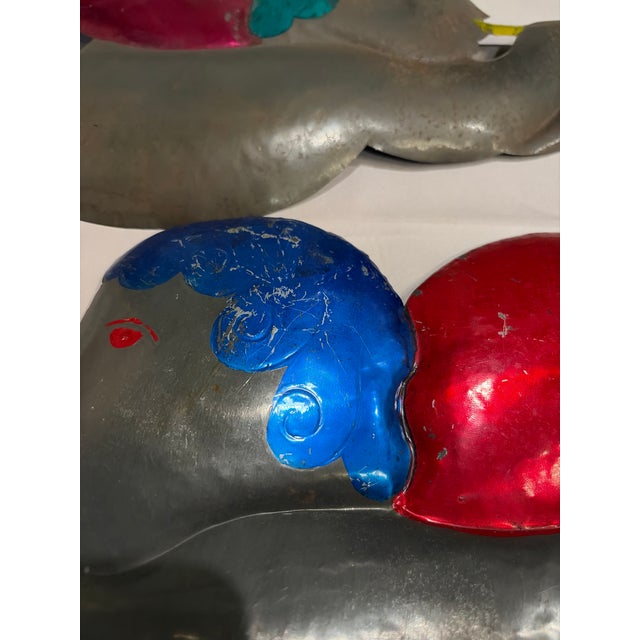 A colorful pair of vintage tin cherubs depicted in flight, each playing a gold-colored trumpet. These large decorative...