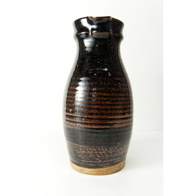A studio pottery ceramic hand thrown pitcher with a black and rusty brown glaze. Signed on the bottom "GOS"