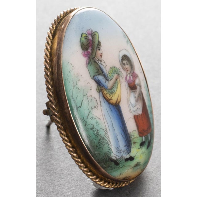 Antique 9K Yellow Gold Oval Hand-Painted Porcelain Brooch, depicting two young maidens in period clothing surrounded by...