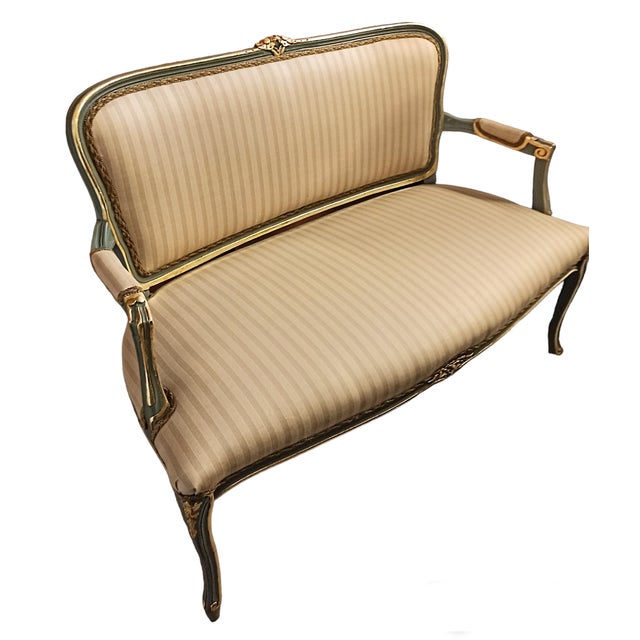 A shapely, two-seater sofa in the French style. Upholstered with beige fabric with vertical stripes. Wooden elements in...