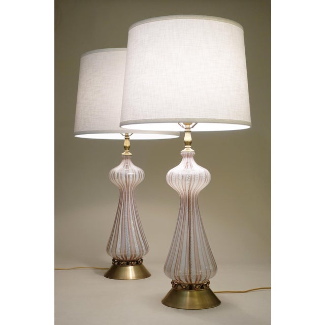 A pair of sculpturally sensual hand blown controlled Latticino White Art Glass and Brass table lamps designed and...