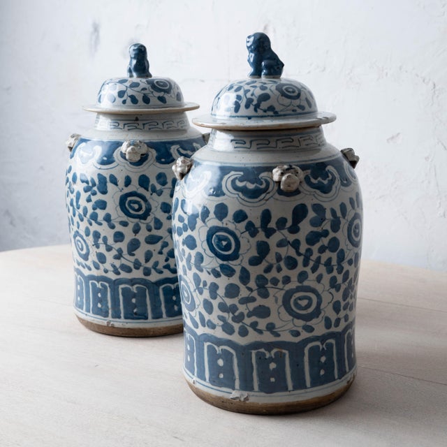 A pair of Chinese blue and white glazed stoneware jars, each with a domed lid surmounted by a seated Buddhist lion, or foo...