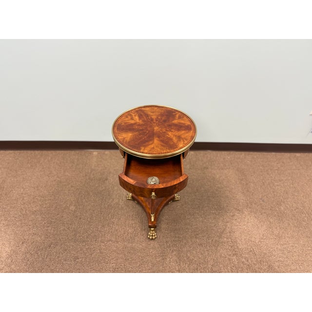 Elegant round pedestal accent table featuring rich wood veneer, a brass gallery edge, and tripod base with brass claw...