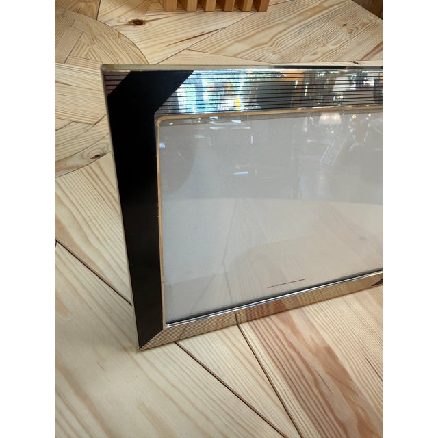 A rectangular picture frame with glossy black corner accents, fine ribbed detailing, and a slim silver border around the...