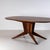 Large dining table with an oval top and a four-legged base featuring bronze sabots and a disc-shaped detail on the central...
