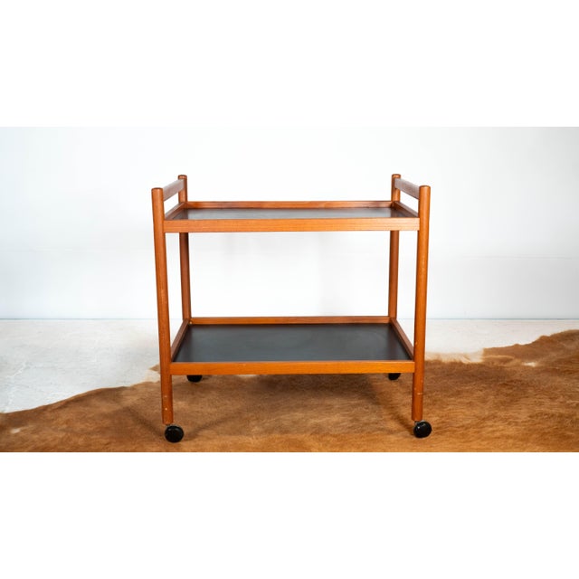 Danish Modern Dyrlund teak bar cart, circa 1970s. Two tiered, bright teak construction with black laminate tops. Rolling...