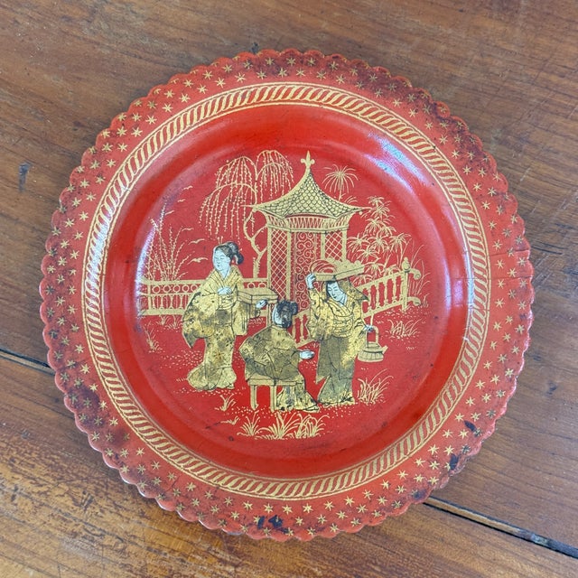 A single red lacquered papier mache wine coaster with a scalloped rim, decorated in gilt with three figures in a garden by...