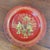 A single red lacquered papier mache wine coaster with a scalloped rim, decorated in gilt with three figures in a garden by...