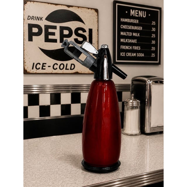 Glossy red vintage soda siphon with black and chrome top assembly, styled with bold retro café character. A striking bar...